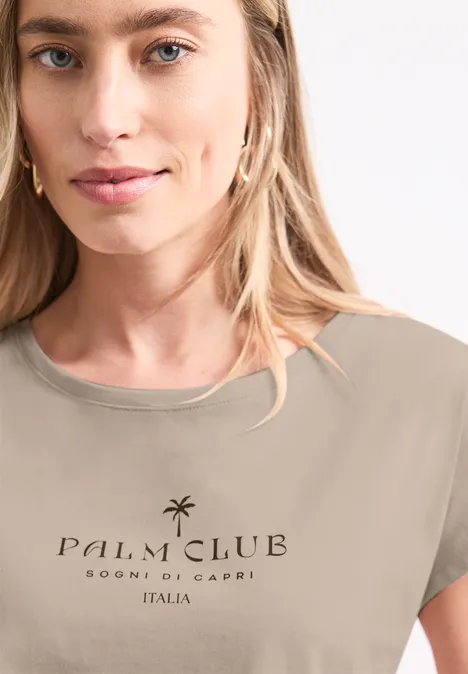 Koszulka na ramiączkach z napisem clay sand Osoba ma na sobie beżowy t-shirt z napisem 'Palm Club Sogni di Capri Italia' i motywem palmy.