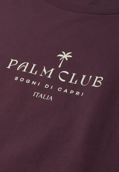 Dropped Shoulder Shirt mit Wording rustic rouge Ein dunkelrotes T-Shirt mit der Aufschrift 'Palm Club', einem Palmenlogo und 'Sogni di Capri Italia'.