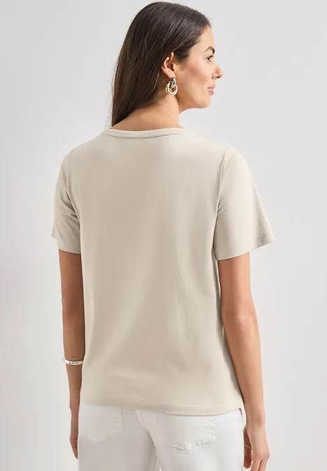 Vrouw van achteren in een beige T-shirt en witte broek, met halflang donker haar.