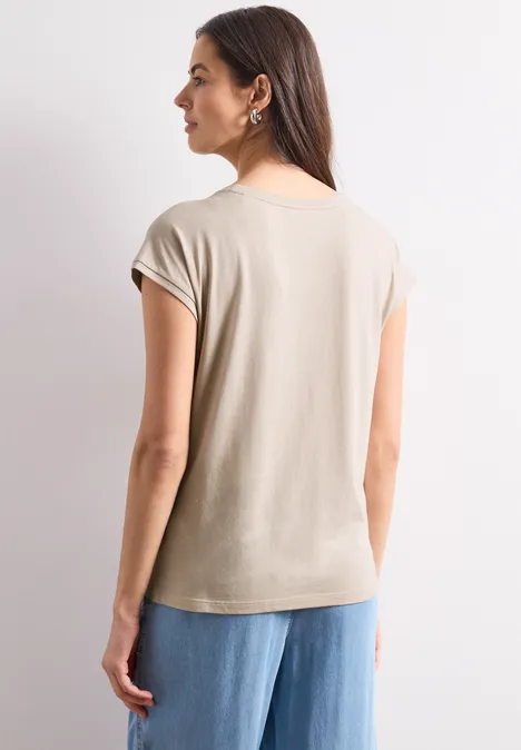 Vrouw van achteren in beige T-shirt met korte mouwen en wijde blauwe jeans, neutrale achtergrond.