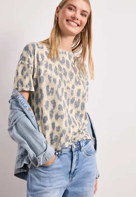 Femme en t-shirt à imprimé léopard et jean clair, veste en jean décontractée sur l’épaule.
