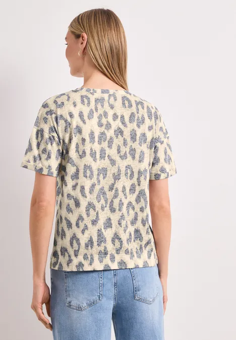 Femme de dos en t-shirt clair à motif léopard bleu-gris et jean clair sur fond blanc.
