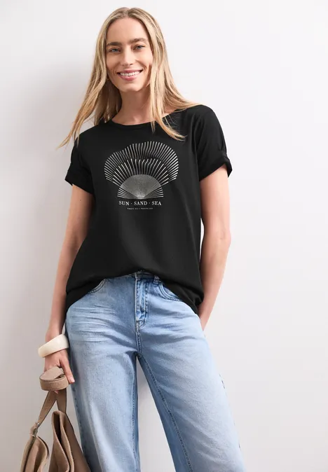 Frau trägt schwarzen Print-T-Shirt, blaue Jeans und hält eine braune Tasche.