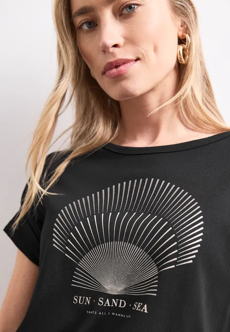 Frau im schwarzen T-Shirt mit goldenem Sonnenstrahlen-Print und Schriftzug 'SUN - SAND - SEA'.