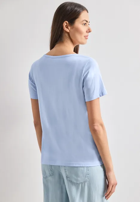 Eine Frau steht mit dem Rücken zur Kamera und trägt ein hellblaues T-Shirt und Jeans.