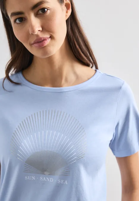 Frau in hellblauem T-Shirt mit Sonnengrafik und 'Sun Sand Sea'-Schriftzug.