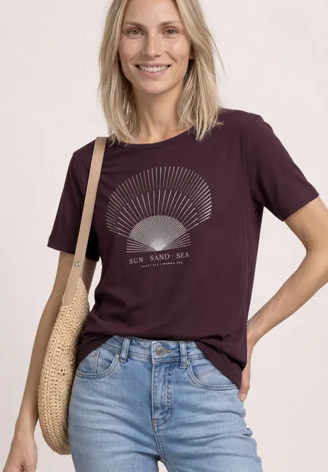 T-Shirt mit Rundhals und Foliendetails rustic rouge Frau in lila T-Shirt mit Muschelprint und Jeans, trägt Korbtasche.