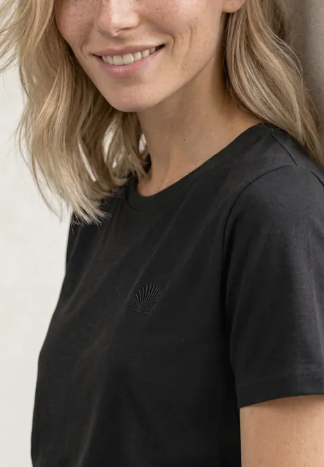 T-Shirt mit Rundhals und Embroidery Detail Black Portrait einer lächelnden Frau mit blonden Haaren in schwarzem T-Shirt vor hellem Hintergrund.