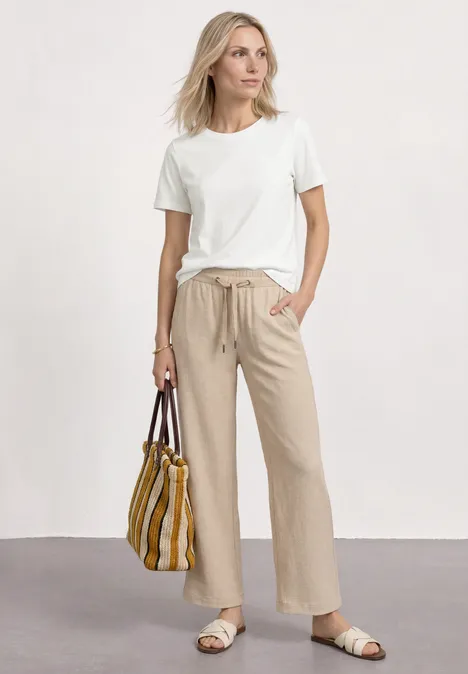 Koszulka z okrągłym dekoltem i haftowanymi detalami off white Elegancka kobieta w białym T-shircie, beżowych spodniach, sandałach z paskowaną torbą.