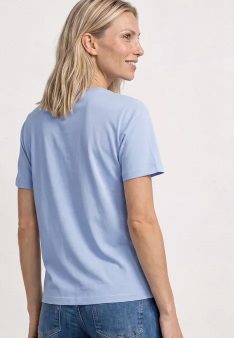 Achteraanzicht van een persoon in een lichtblauw T-shirt en spijkerbroek, neutrale achtergrond.
