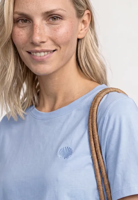 Vrouw draagt lichtblauw t-shirt met klein logo en een schoudertas.