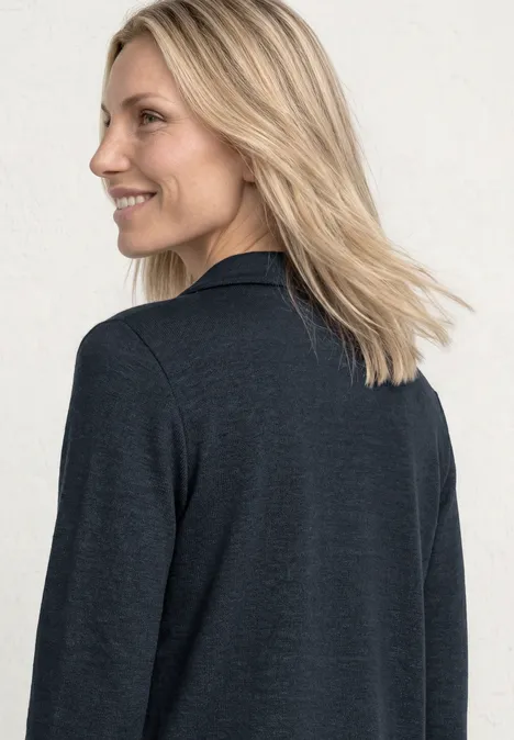 Femme de dos, veste gris foncé, cheveux blonds, fond blanc.