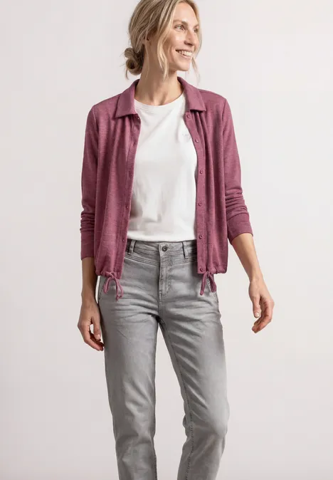 Femme en jean gris, t-shirt blanc et gilet rose devant un fond clair
