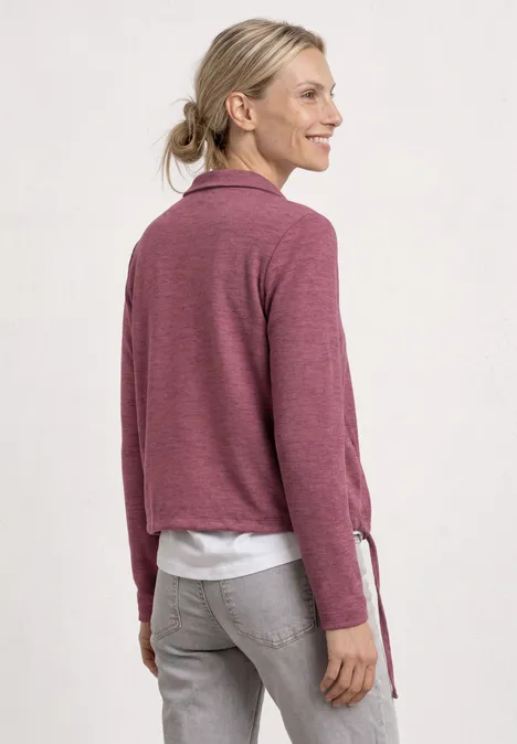 Femme vue de dos portant un pull rose, un top blanc et un jean gris, cheveux blonds en queue de cheval.