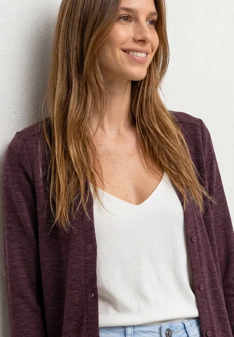 Femme aux cheveux mi-longs portant un débardeur blanc et un gilet bordeaux.