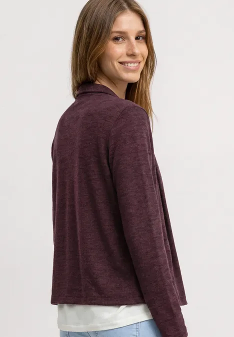 Femme de profil portant un gilet bordeaux sur un t-shirt blanc, fond neutre.