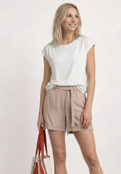 Frau in weißem T-Shirt und beigen Shorts trägt rote Schultertasche.