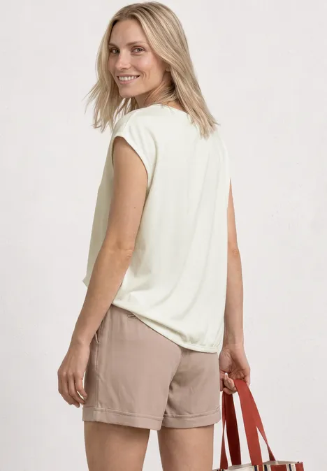 Frau von hinten in beigem Shirt und Shorts, trägt rote Tasche.