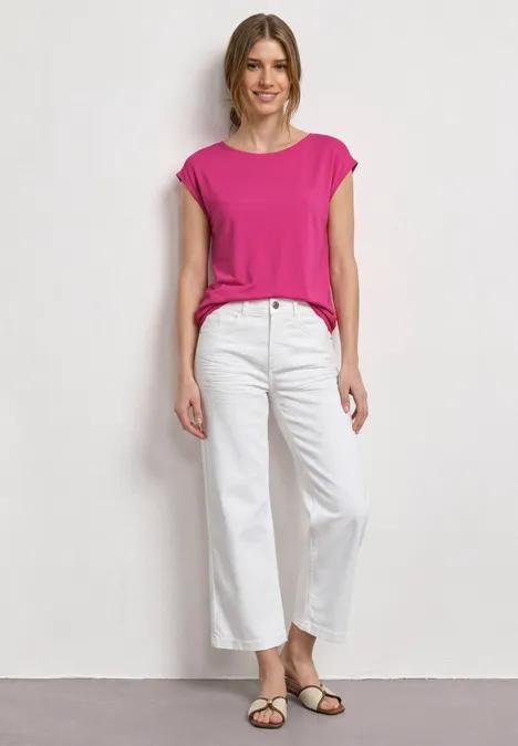 Dropped Shoulder Shirt mit U-Boot-Ausschnitt magenta dream Eine Frau trägt ein pinkes Top, weiße Hosen und Sandalen vor neutralem Hintergrund.