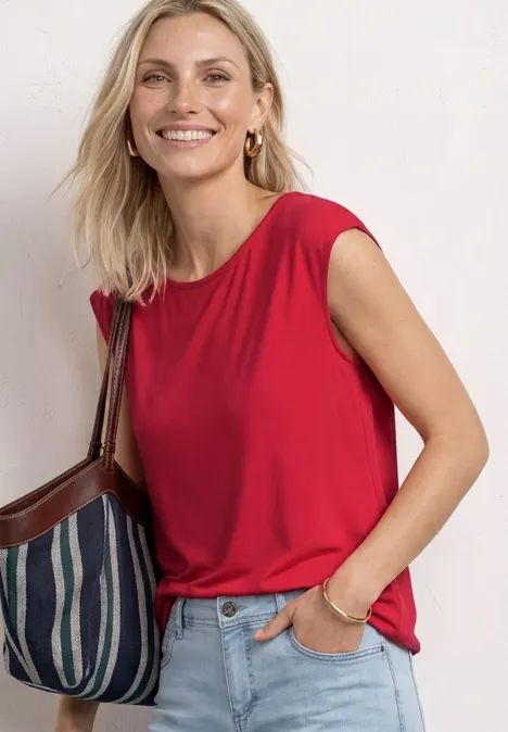 Dropped Shoulder Shirt mit U-Boot-Ausschnitt salsa red Frau in rotem ärmellosem Top, Jeans und gestreifter Schultertasche.