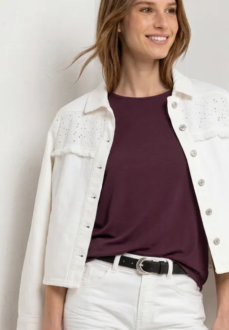 Plan rapproché d'une personne portant une veste jean blanche brodée, un T-shirt violet et une ceinture noire.