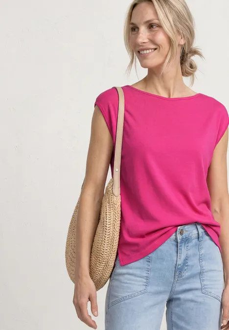 Basic Shirt mit U-Boot-Ausschnitt magenta dream Eine Frau trägt ein pinkes ärmelloses Top, helle Jeans und eine geflochtene Strohtasche.