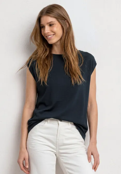 Basic Shirt mit U-Boot-Ausschnitt shadowed navy Eine Frau in schwarzem ärmellosem Oberteil und weißer Jeans steht vor weißer Wand.