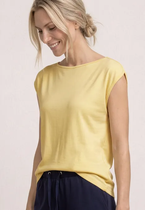 Basic Shirt mit U-Boot-Ausschnitt soft yellow Schlanke Frau trägt gelbes ärmelloses Oberteil und dunkelblaue Hose vor neutralem Hintergrund.