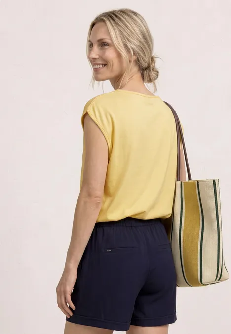 Basic Shirt mit U-Boot-Ausschnitt soft yellow Frau von hinten in gelbem Top, blonden Haaren und dunklen Shorts, trägt gestreifte Tasche.