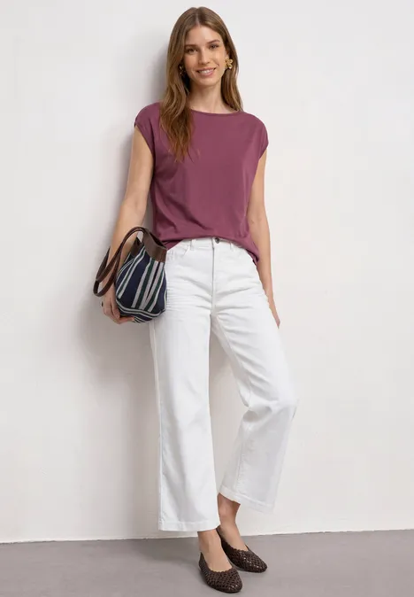 Basic Shirt mit U-Boot-Ausschnitt dark clouded blush Person in lila Top, weißen weiten Hosen und dunklen Schuhen mit gestreifter Tasche vor weißer Wand.