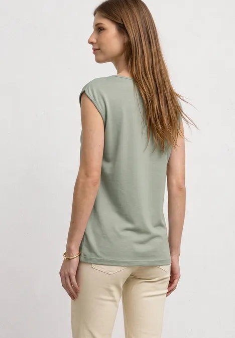 Basic Shirt mit U-Boot-Ausschnitt mint leaf Frau von hinten in locker sitzendem, ärmellosem grünen Shirt und beigen Hosen vor hellem Hintergrund.