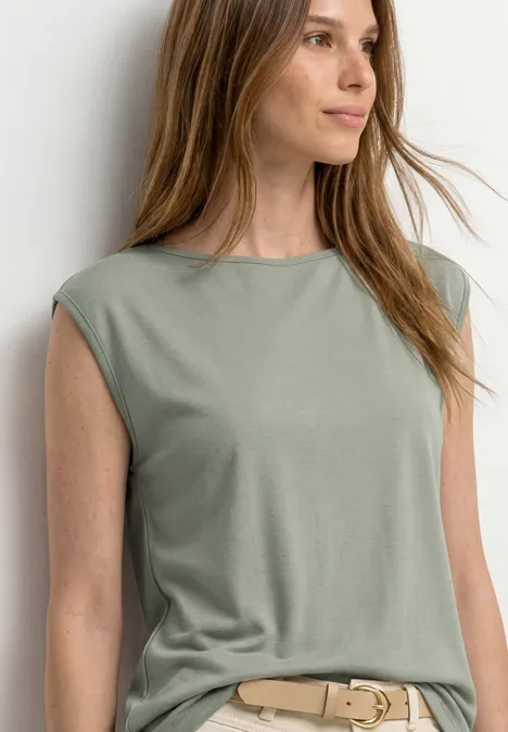 Basic Shirt mit U-Boot-Ausschnitt mint leaf Eine Frau trägt ein ärmelloses olivgrünes Top mit beigem Gürtel vor einer hellen Wand.