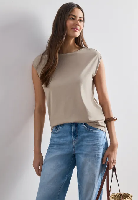 Basic Shirt mit U-Boot-Ausschnitt sepia sand Frau in ärmellosem beigefarbenem Top und blauen Jeans hält eine braune Tasche.