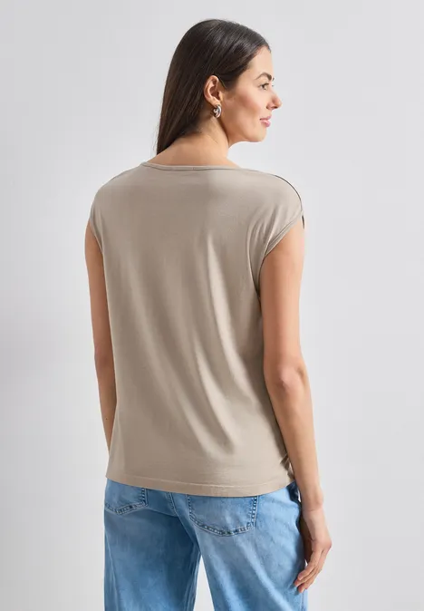 Basic Shirt mit U-Boot-Ausschnitt sepia sand Eine Frau mit langen dunklen Haaren steht von hinten, trägt ein beiges Top und blaue Jeans vor hellem Hintergrund.