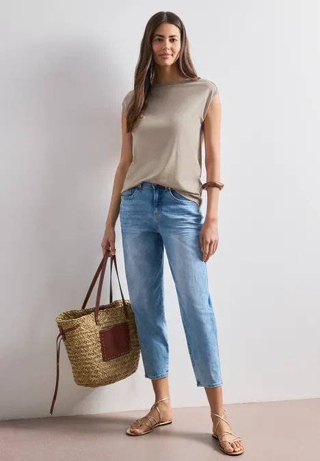 Basic Shirt mit U-Boot-Ausschnitt sepia sand Frau in beigem Top, blauen Jeans, Sandalen und großer Korbtasche vor neutralem Hintergrund.