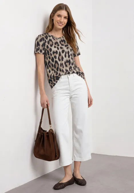 T-Shirt mit Rundhals und gerafftem Ärmel timeless beige Frau lehnt an weißer Wand, trägt Leoparden-Shirt, weiße Culotte, braune Tasche und Schuhe.
