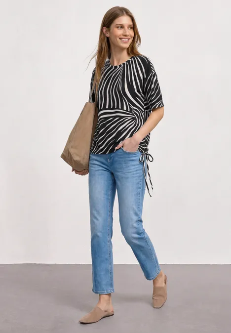 Vrouw met zebraprinttop, blauwe jeans, beige loafers en grote tas
