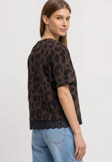 Een vrouw staat opzij en draagt een bruin luipaardprint shirt met korte mouwen en een lichtblauwe jeans.