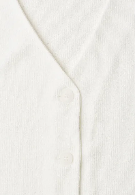 Nahaufnahme eines weißen Strickcardigans mit V-Ausschnitt und zwei Knöpfen.