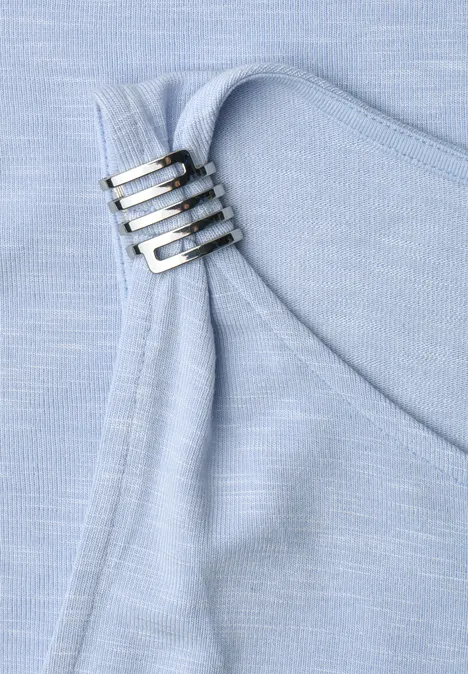 Nahaufnahme eines hellblauen Stoffs mit vier silbernen Schnallen an einem Träger.