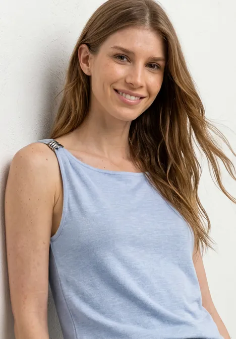 Junge Frau posiert in einem hellblauen ärmellosen Top vor hellem Hintergrund.