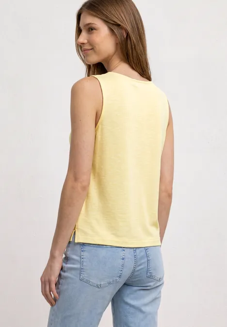 Eine Frau von hinten in einem gelben ärmellosen Top und hellblauen Jeans.