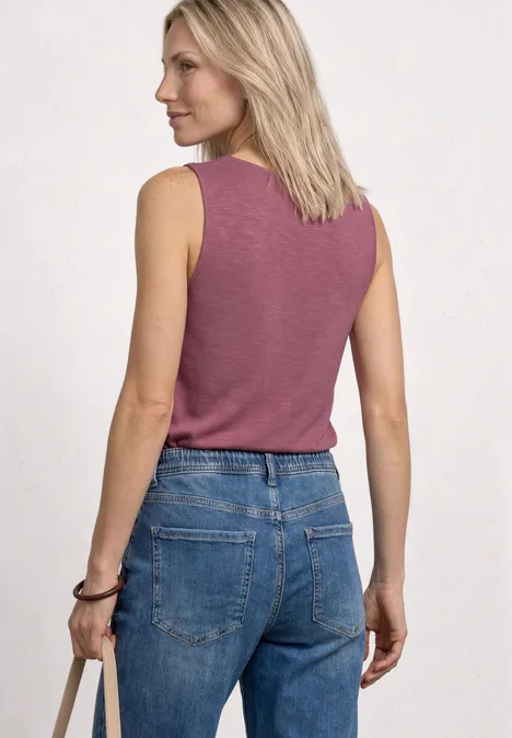 Frau von hinten in ärmellosem rosa Top und blauer Jeans.