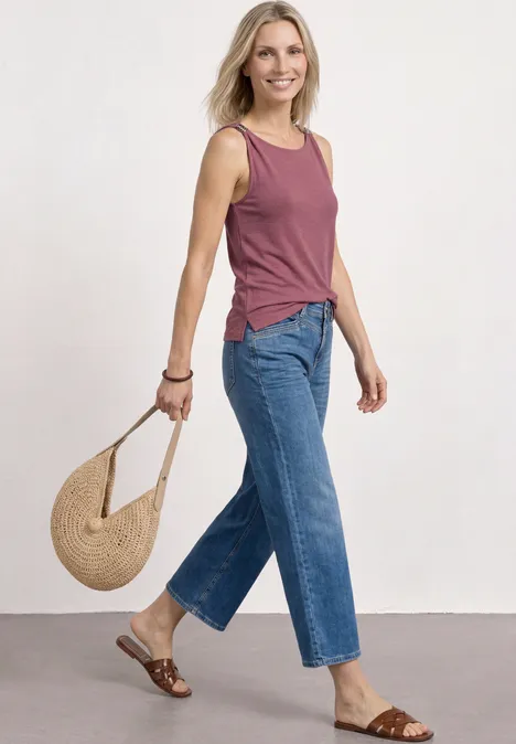 Frau in rosafarbenem Top, blauen Jeans, mit Strohtasche und Sandalen