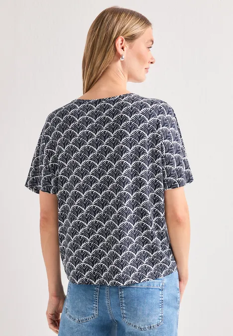 Femme de dos portant un t-shirt à motif d'arcs noir et blanc, un jean bleu et une queue de cheval.