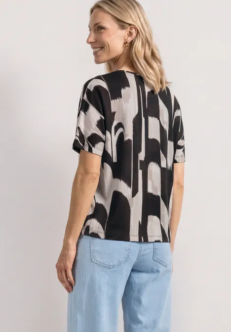 Achteraanzicht van een vrouw in een zwart-wit grafisch shirt en lichtblauwe spijkerbroek.