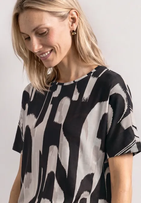 Vrouw met blond haar draagt loszittend T-shirt met abstract zwart-wit patroon.