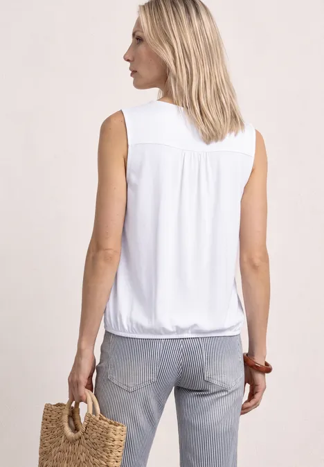 Frau von hinten in ärmelloser weißer Bluse und Jeans, trägt handgeflochtene Tasche.