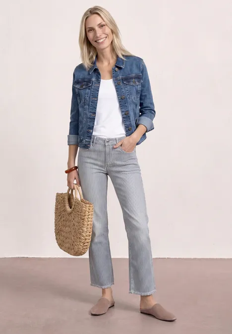 Frau in Jeansjacke, weißem Top, grauen Jeans, beigen Slippern und geflochtener Tasche.