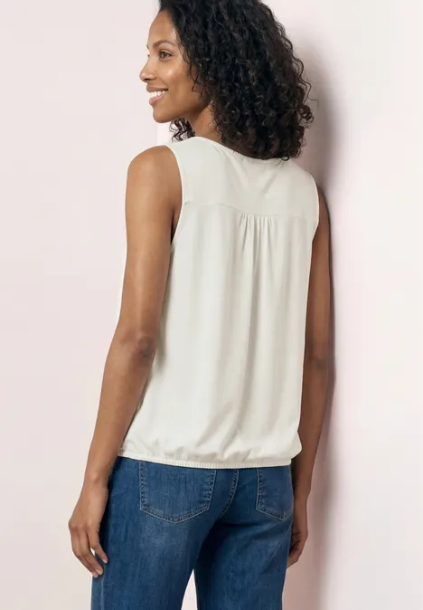 Top aus Jersey mit Elastiksaum off white Eine Frau von hinten in weißer ärmelloser Bluse und blauen Jeans vor hellrosa Wand.